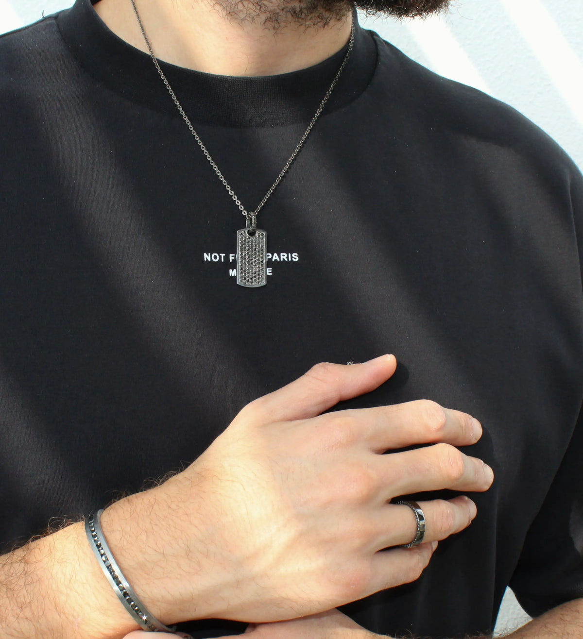 Person wearing a black shirt with text, silver necklace, and ring.