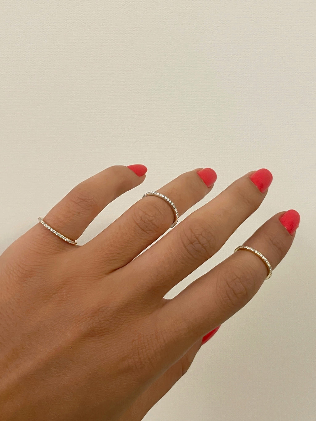 Hand wearing two gold rings with red nail polish on a neutral background